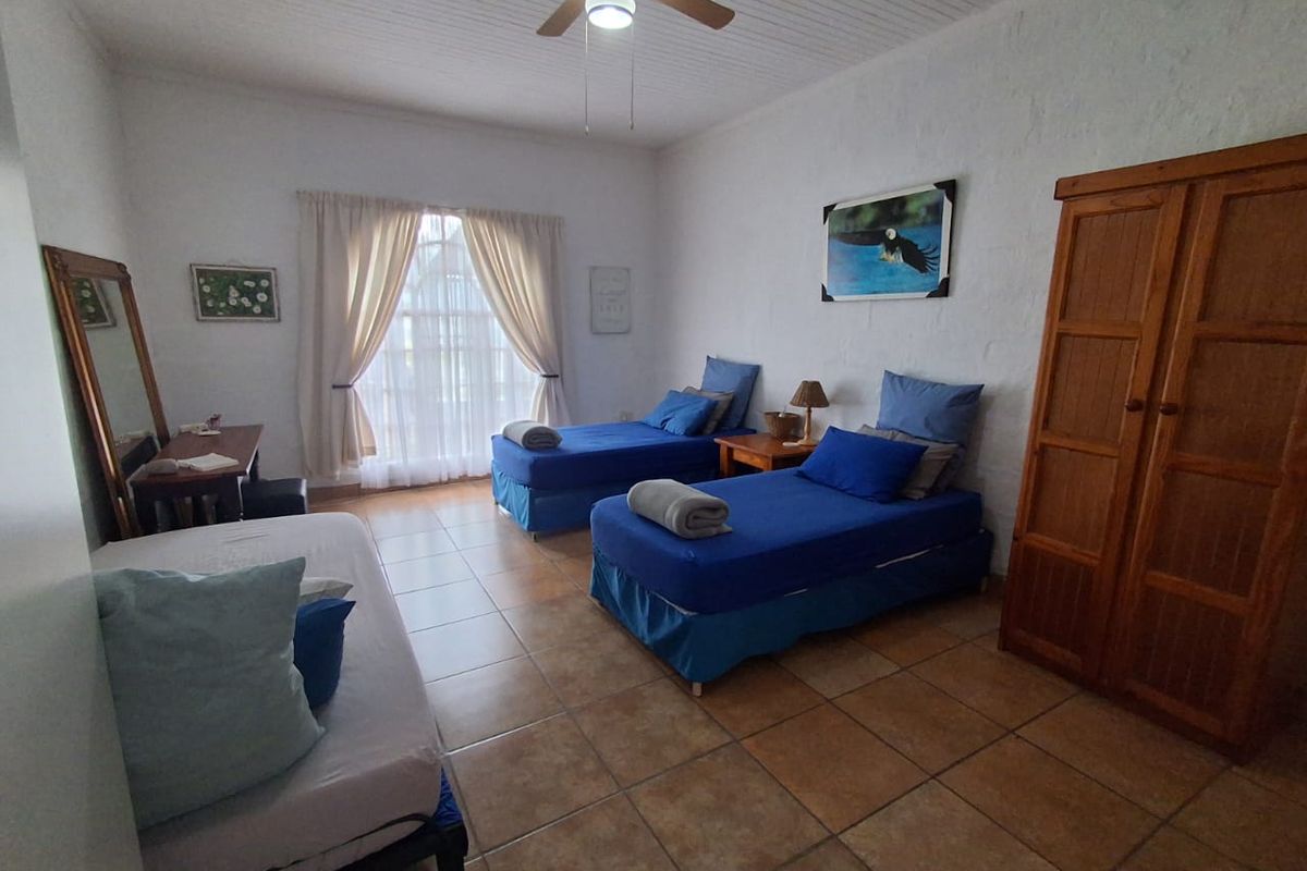 A spacious bedroom featuring tiled flooring, a ceiling fan, and a built-in timber wardrobe, offering a functional layout with ample natural light.