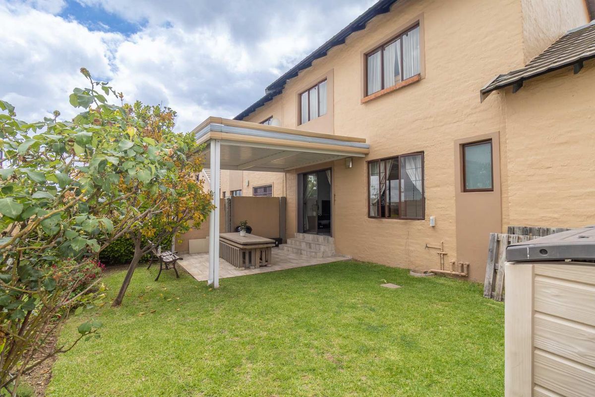 Rear view of the townhouse featuring a covered patio area, paved flooring, and a private garden space with established landscaping.