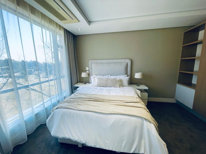 A well-maintained bedroom featuring built-in shelving, recessed ceiling lighting, ducted air conditioning, and a large window providing natural light.