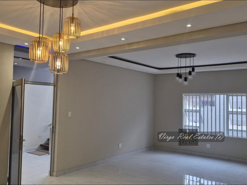 Spacious living area featuring modern recessed and cove lighting, tiled floors, and large windows with security bars.