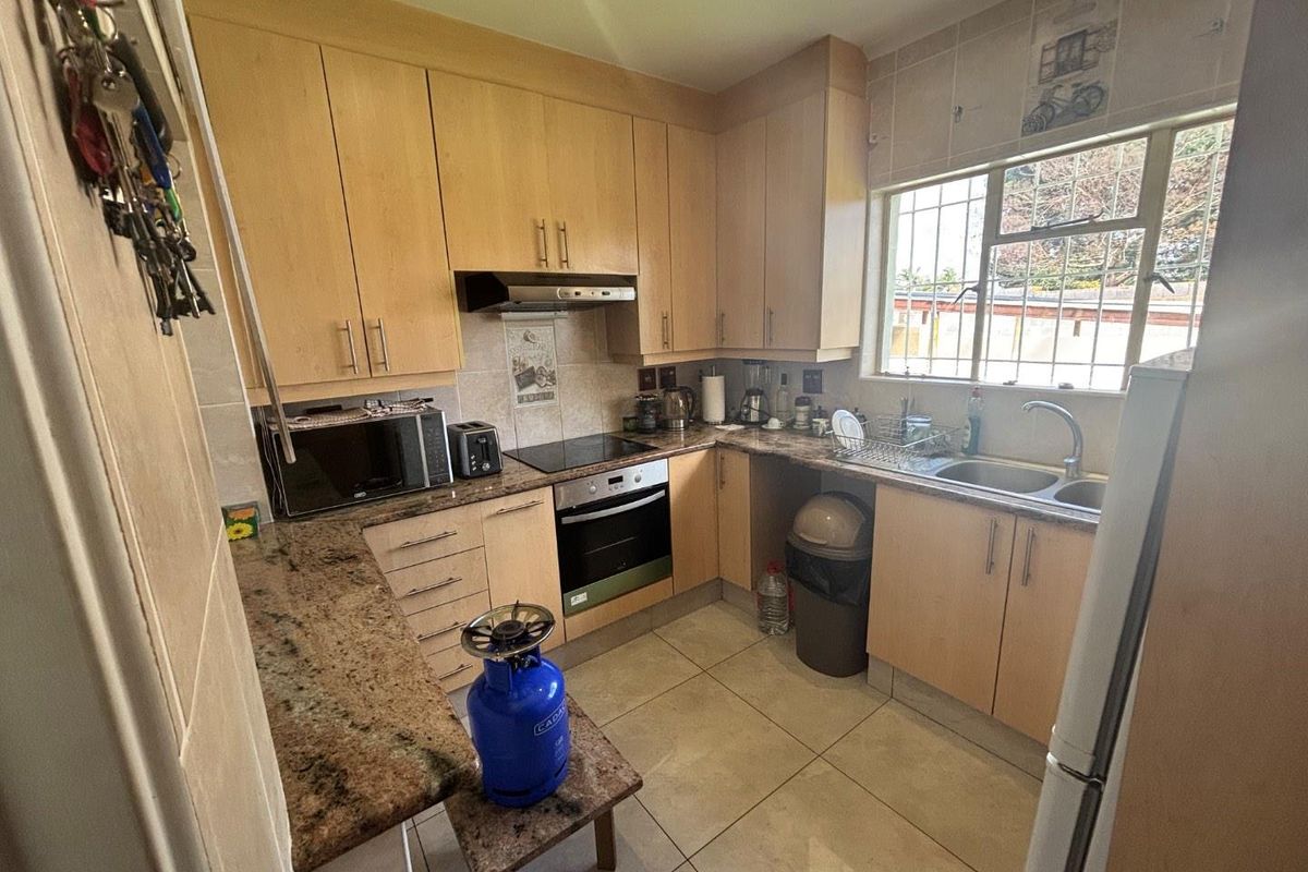 Functional kitchen featuring light wood cabinetry, granite countertops, integrated oven, hob, extractor fan, and a double basin sink with tiled flooring.