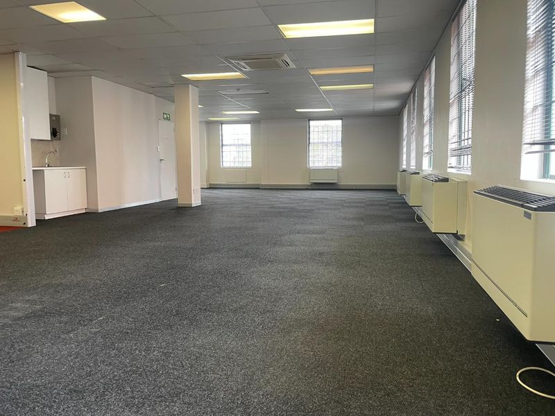 Spacious open-plan office area featuring carpeted flooring, suspended ceilings with recessed lighting, integrated HVAC units, and a compact kitchenette.