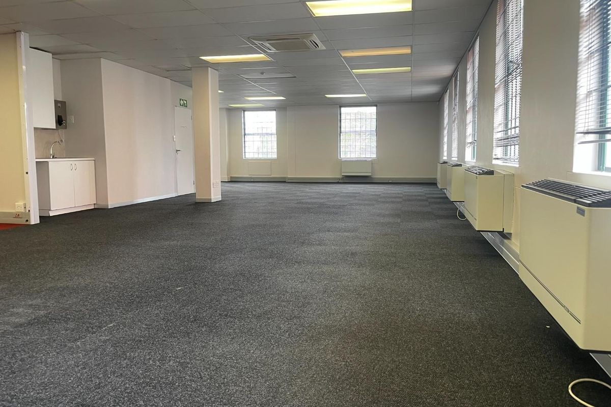 Spacious open-plan office area featuring carpeted flooring, suspended ceilings with recessed lighting, integrated HVAC units, and a compact kitchenette.