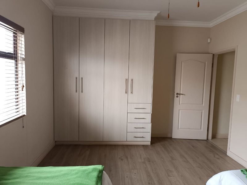 A clean and well-maintained bedroom featuring light wood-tone built-in cupboards, laminate flooring, and neutral wall finishes.