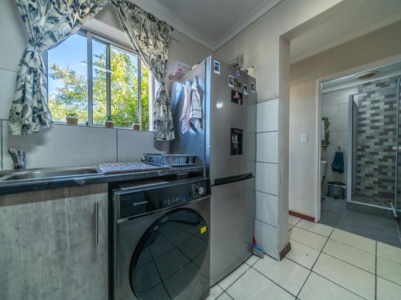Functional laundry area featuring built-in cabinetry, a stainless steel sink, and tiled finishes, with direct access to an adjacent bathroom.