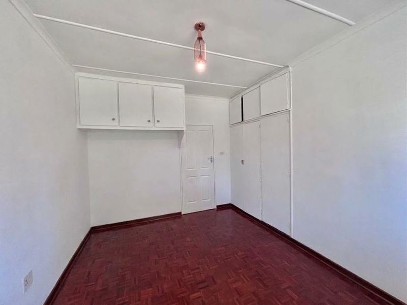 A clean, empty bedroom featuring classic parquet flooring and ample built-in cupboard storage with additional overhead cabinets.