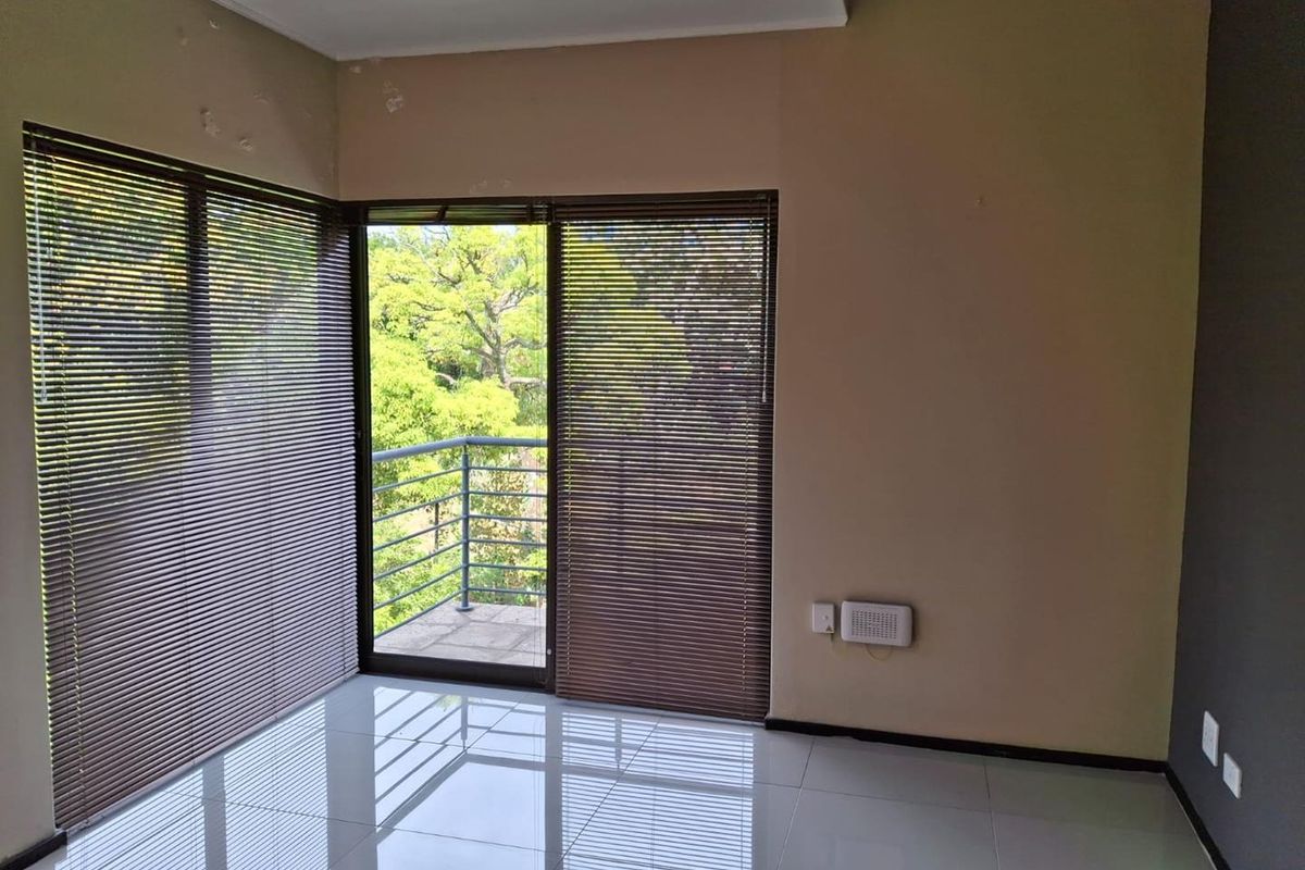 An empty bedroom featuring tiled flooring, sliding glass doors leading to a balcony, and venetian blinds, offering a bright and functional living space.