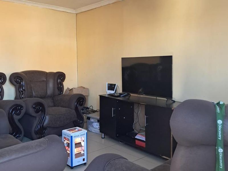 A living room featuring tiled flooring and visible ceiling water damage, offering a functional space that could benefit from cosmetic updates and repairs.