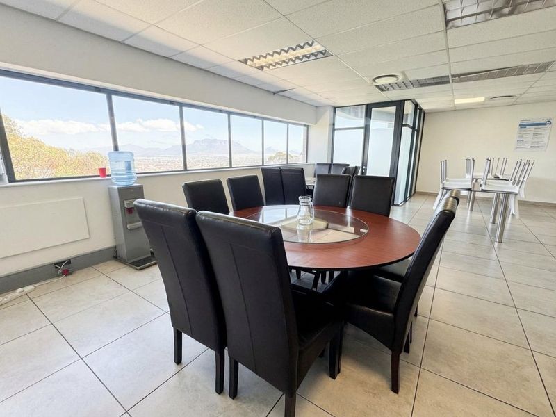 A bright office space featuring tiled flooring, a suspended ceiling with recessed lighting, and large windows offering expansive views.