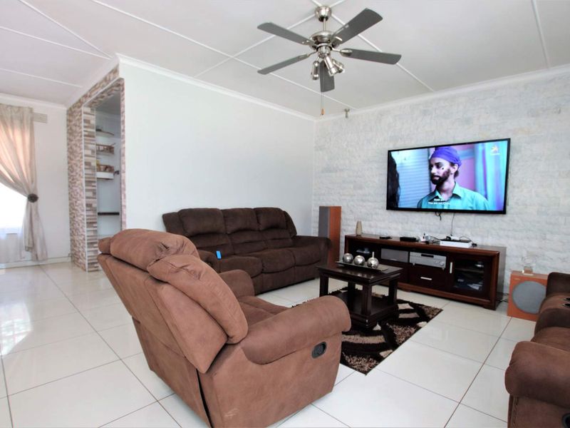 Spacious living room featuring a stone veneer accent wall, tiled flooring, and a ceiling fan, offering a comfortable and well-maintained living space.
