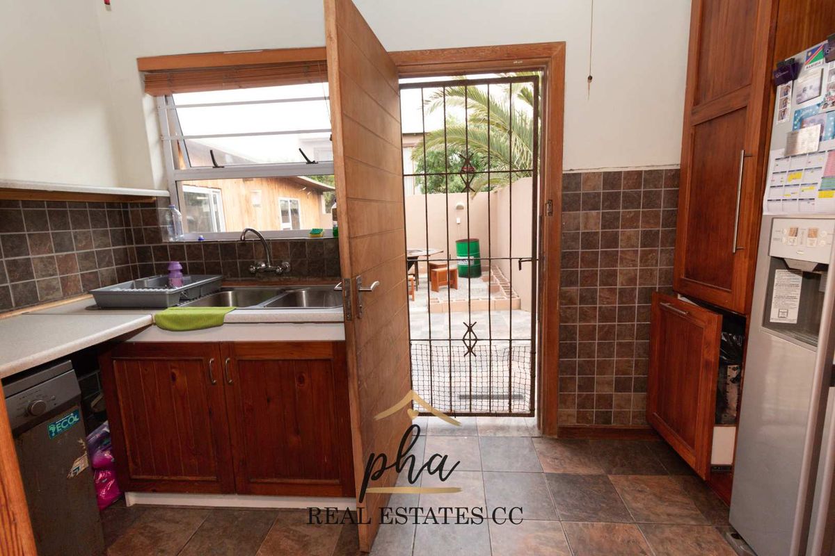 A functional kitchen featuring wooden cabinetry, tiled splashbacks, and a double bowl sink, with direct access to an outdoor patio area.