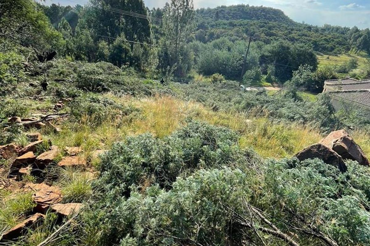 A scenic view of a sloped, undeveloped residential plot featuring natural rock formations and native vegetation with surrounding hillside landscape.