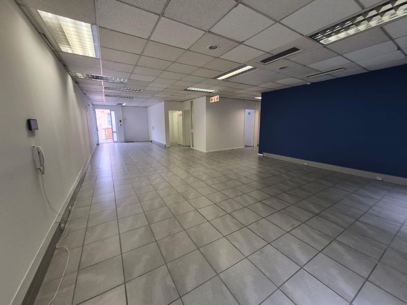 Spacious, empty open-plan office area featuring tiled flooring, suspended ceilings with recessed lighting, and a prominent blue accent wall.