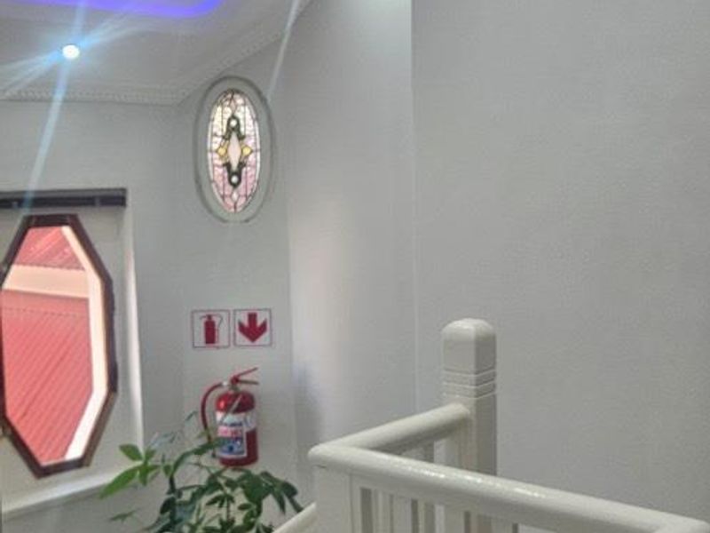 A bright office stairwell featuring a white balustrade, decorative oval stained-glass window, recessed ceiling lighting with purple accent strips, and wall-mounted fire safety equipment.