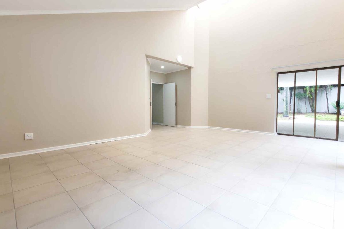 Spacious, light-filled living area featuring high ceilings, neutral tiled flooring, and large sliding glass doors providing direct access to the outdoor patio and garden.