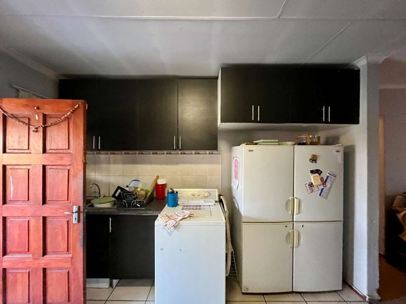 A compact kitchen area featuring dark built-in cabinetry, a tiled backsplash, and tiled flooring, providing a functional space for food preparation and laundry.