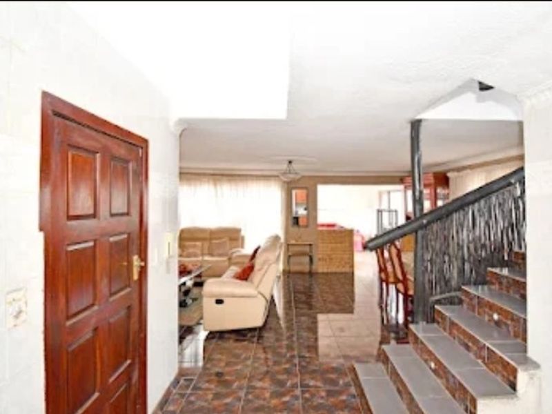 Open plan living area featuring tiled flooring and a staircase with a metal railing, leading into a combined lounge and dining space.