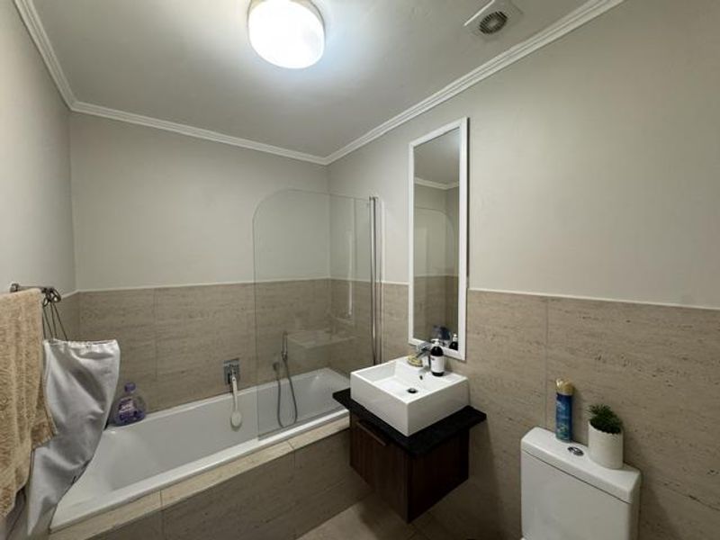 A modern bathroom featuring a bathtub with a glass screen, a wall-mounted vanity with a vessel sink, and a toilet.