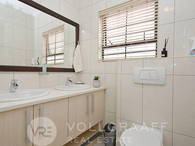 A modern bathroom featuring a double vanity with integrated sinks, wall-mounted toilet, and floor-to-ceiling tiling.