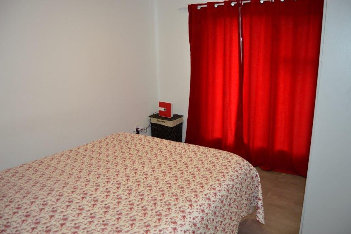 A bedroom featuring tiled flooring and a window dressed with red curtains.