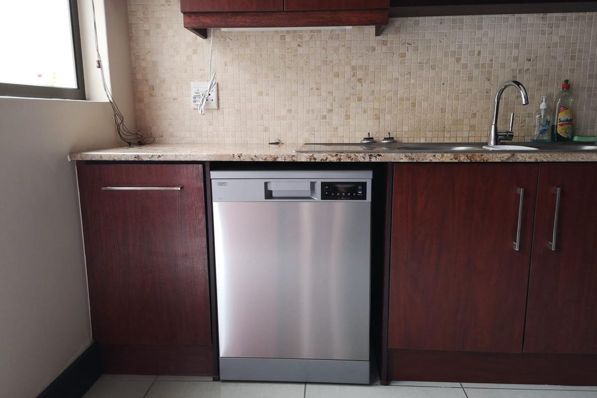 A functional kitchen area featuring dark wood cabinetry, granite countertops, a mosaic tile backsplash, and a built-in stainless steel dishwasher.