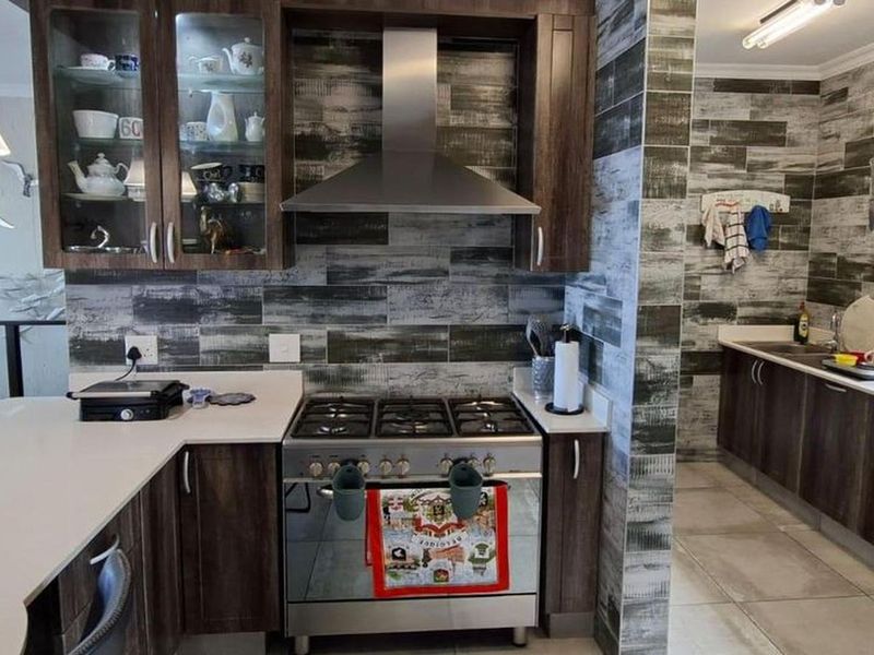 Modern kitchen featuring dark wood cabinetry, stone countertops, a gas stove with stainless steel extractor, and decorative tiled backsplash.