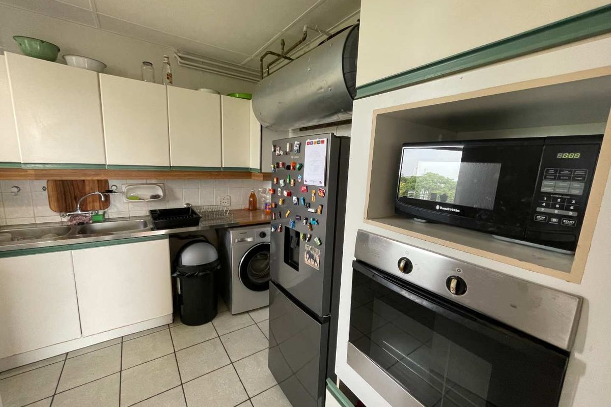 A functional kitchen featuring built-in cabinetry, integrated oven and microwave, tiled backsplash, and tiled flooring, with exposed water heater infrastructure.