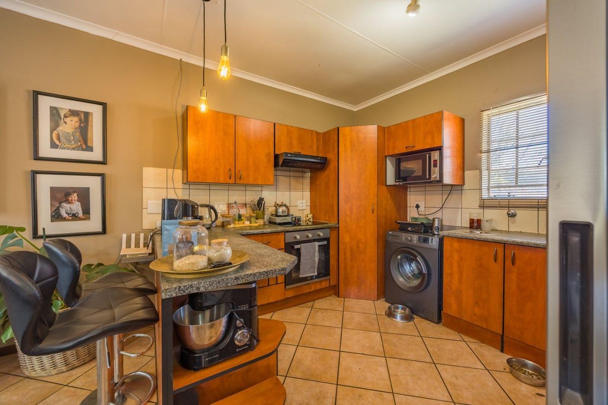 Functional kitchen featuring wood-finish cabinetry, granite countertops, built-in oven, extractor fan, and integrated microwave with tiled flooring and backsplash.