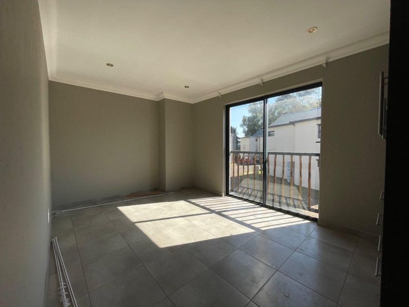 An empty, neutrally painted living room featuring large sliding glass doors, tiled flooring, and recessed lighting, offering a bright and versatile living space.