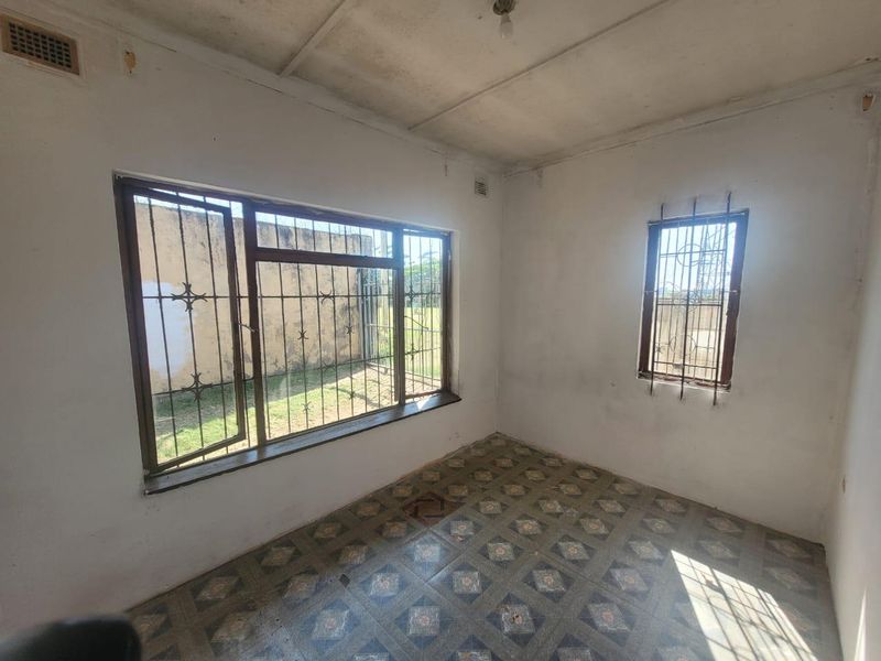 An empty bedroom featuring patterned floor tiles, security bars on windows, and a ventilation grille, requiring cosmetic updates to improve its condition.