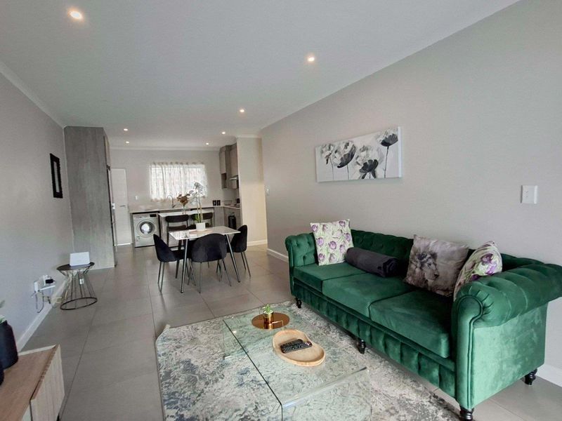 A modern open-plan living and kitchen area featuring neutral tiled flooring, recessed lighting, and a functional kitchen layout with integrated laundry facilities.
