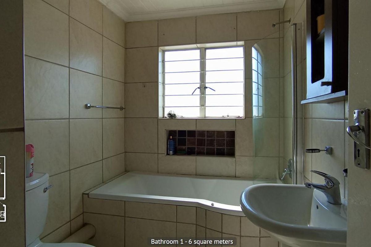 A functional bathroom featuring a bathtub with shower screen, pedestal basin, and toilet, finished with neutral wall tiling and a security-barred window.