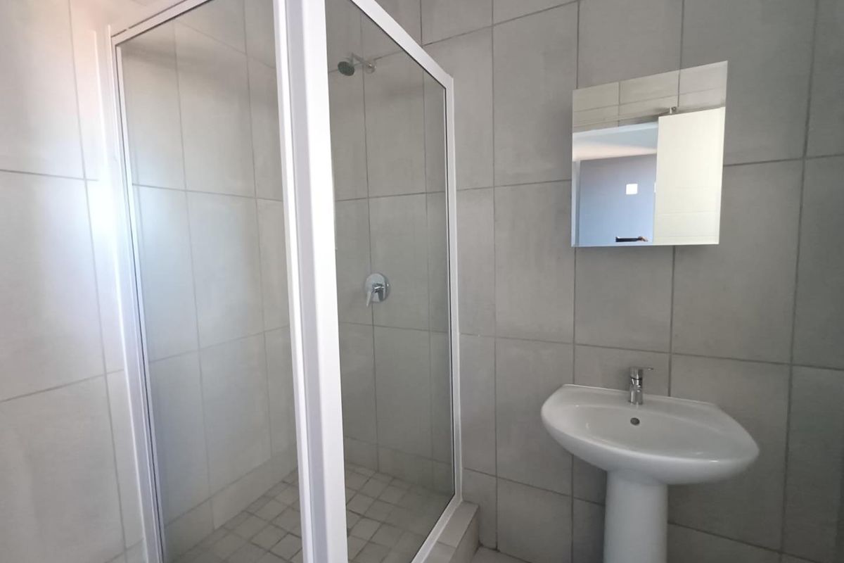 A clean bathroom featuring a glass-enclosed shower, a white pedestal basin, and a wall-mounted mirror with neutral wall tiling.