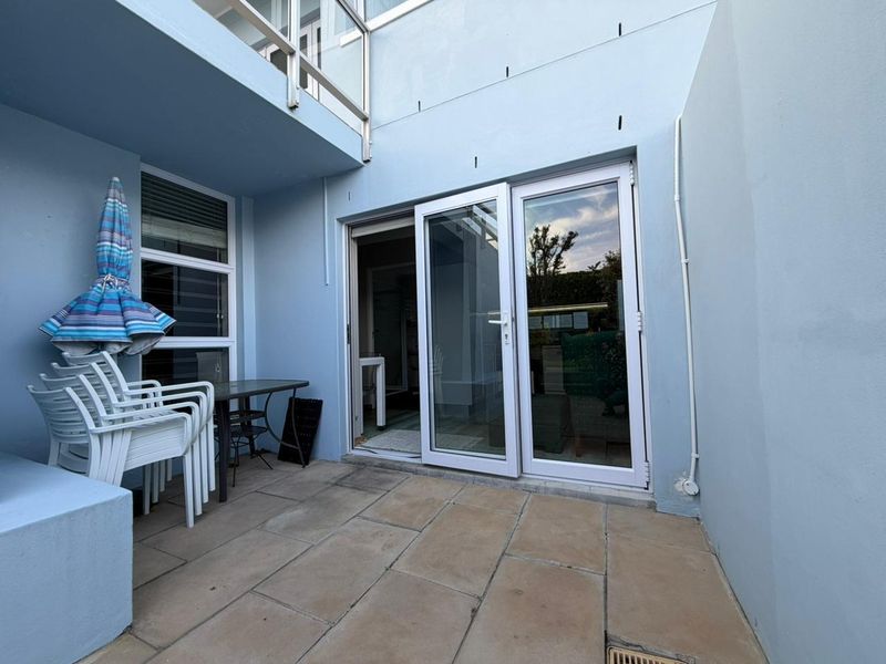A paved outdoor patio area featuring glass sliding doors providing access to the interior, with a balcony overhead.