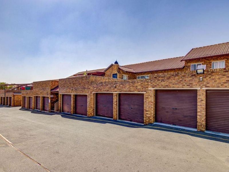 A row of townhouse garages featuring face brick construction, tiled roofing, and roll-up doors, situated along a paved driveway.