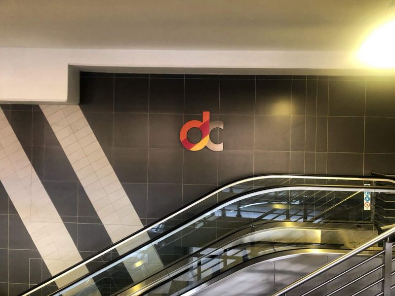 A modern interior space featuring an escalator and decorative tiled wall cladding with corporate branding.
