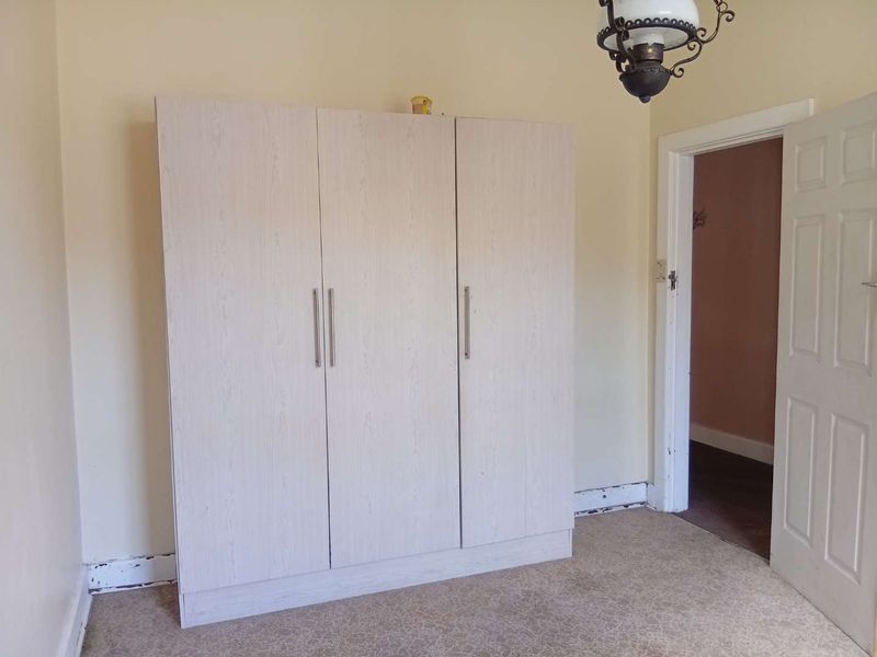 A bedroom featuring a light-toned built-in wardrobe, carpeted flooring, and a doorway leading to an adjacent room.
