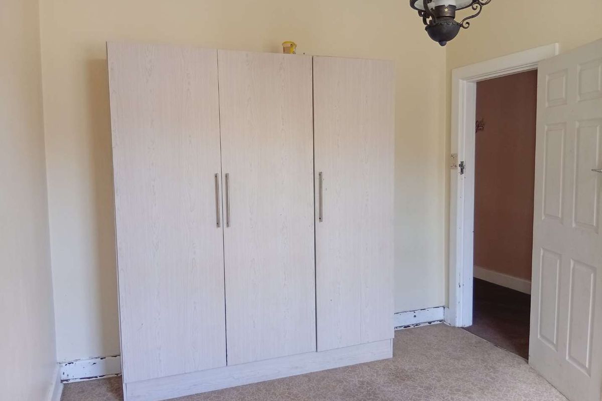 A bedroom featuring a light-toned built-in wardrobe, carpeted flooring, and a doorway leading to an adjacent room.