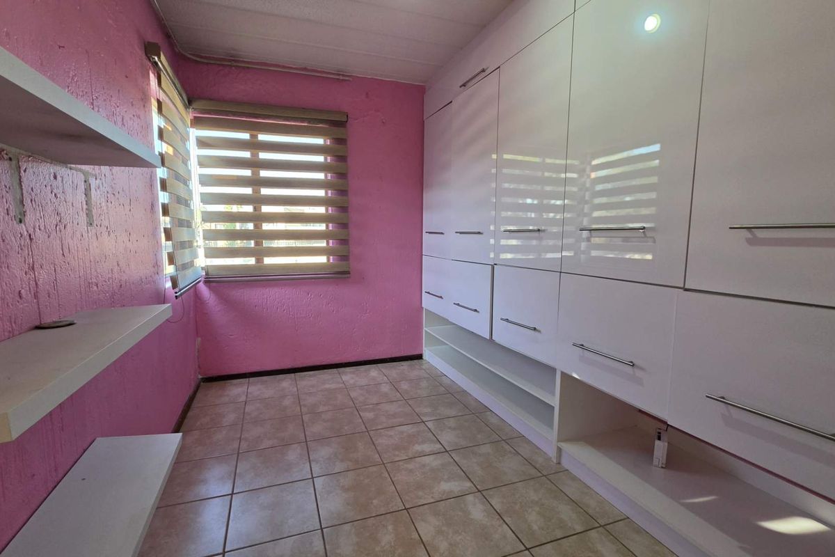 A bedroom featuring built-in white high-gloss cabinetry, tiled flooring, and integrated shelving units against a pink-painted wall.