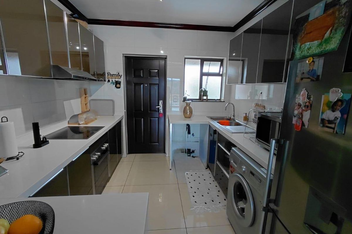 Modern galley-style kitchen featuring high-gloss cabinetry, integrated hob, built-in oven, extractor fan, and tiled flooring with direct access to an exterior door.
