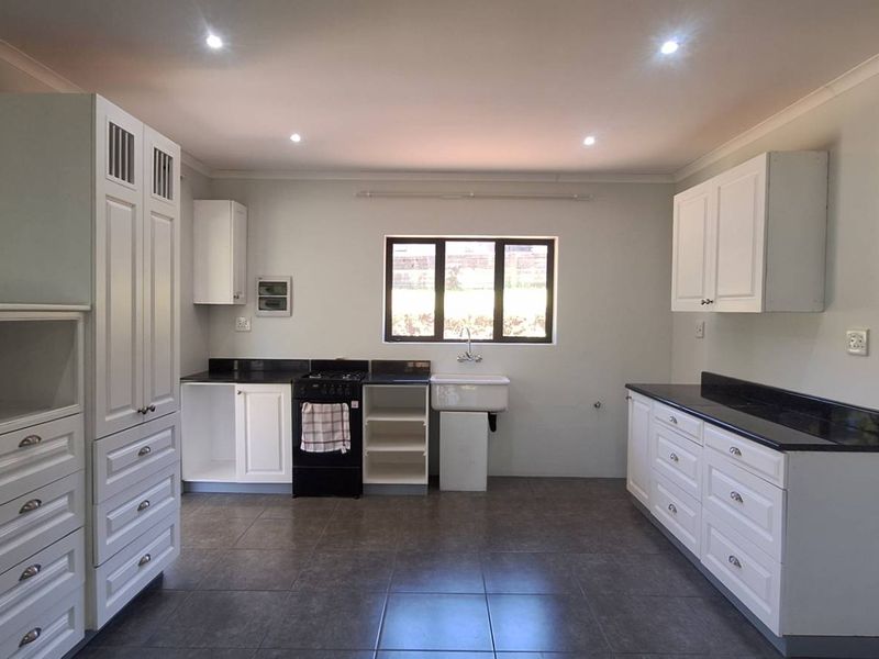 A clean, modern kitchen featuring white cabinetry, dark granite countertops, a farmhouse sink, and tiled flooring with recessed lighting.
