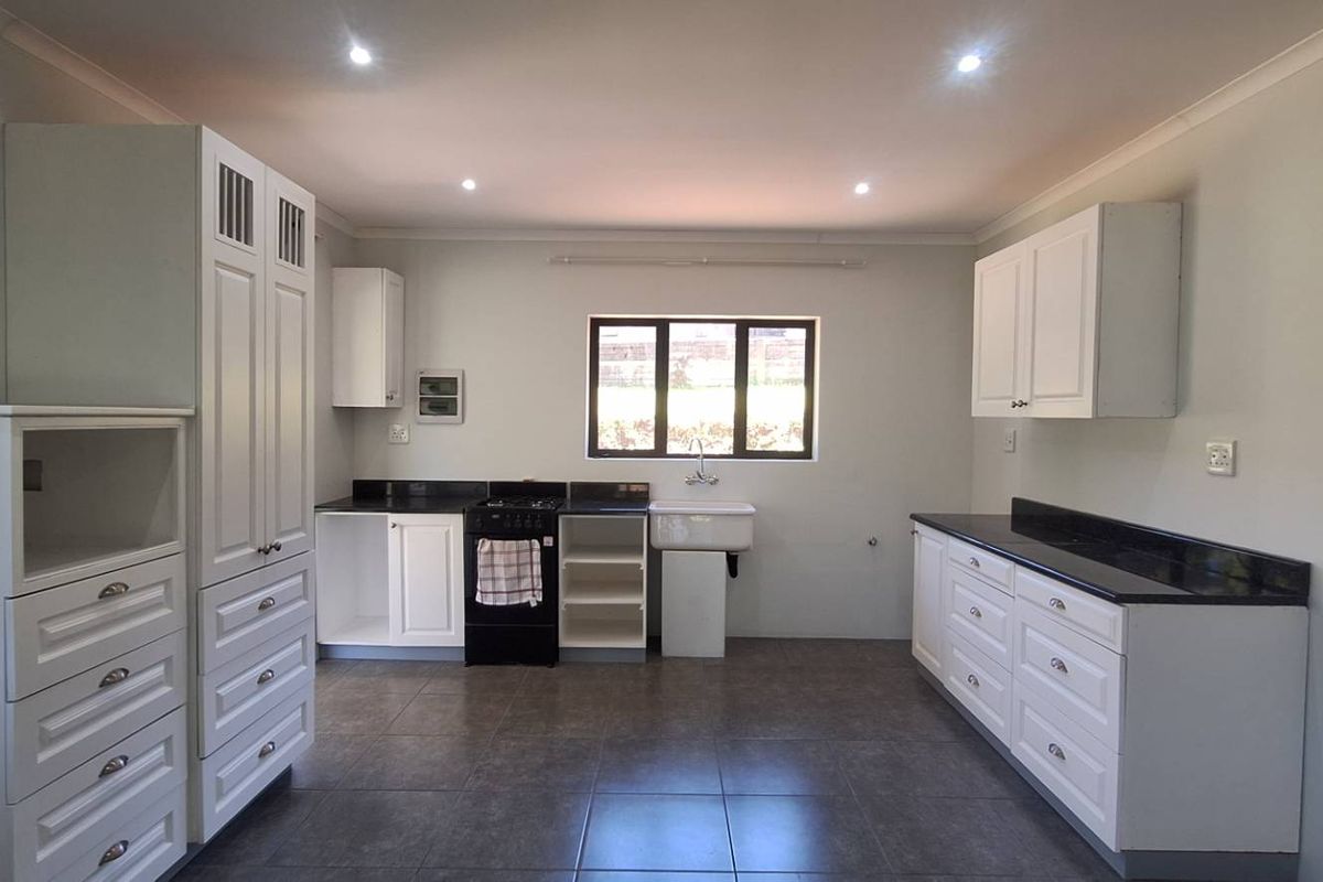 A clean, modern kitchen featuring white cabinetry, dark granite countertops, a farmhouse sink, and tiled flooring with recessed lighting.