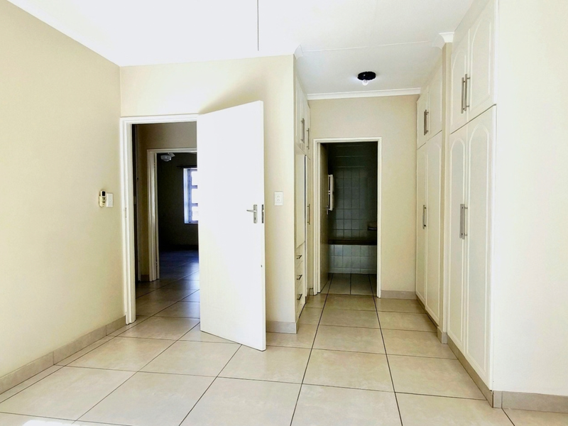 An empty bedroom featuring built-in cupboards, tiled flooring, and direct access to an adjoining room and bathroom area.