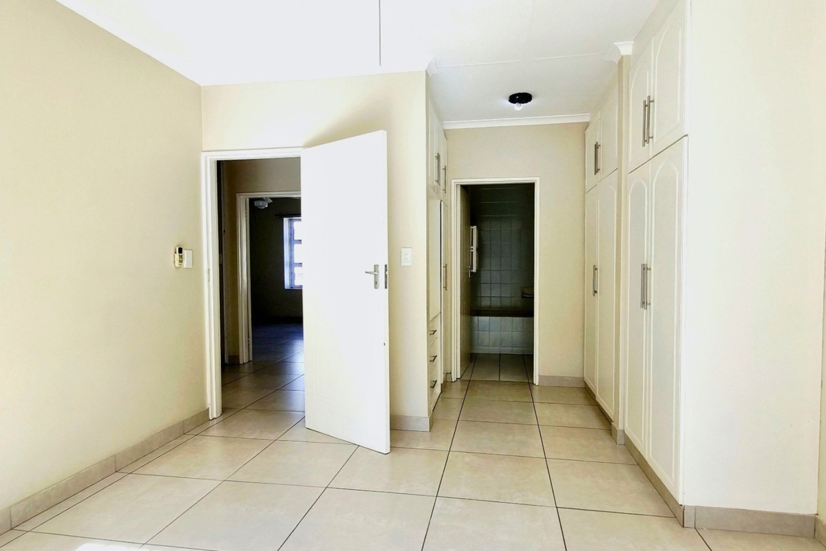 An empty bedroom featuring built-in cupboards, tiled flooring, and direct access to an adjoining room and bathroom area.