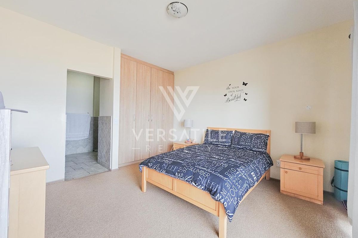 A spacious bedroom featuring built-in wooden cupboards and an adjoining en-suite bathroom area with tiled flooring.