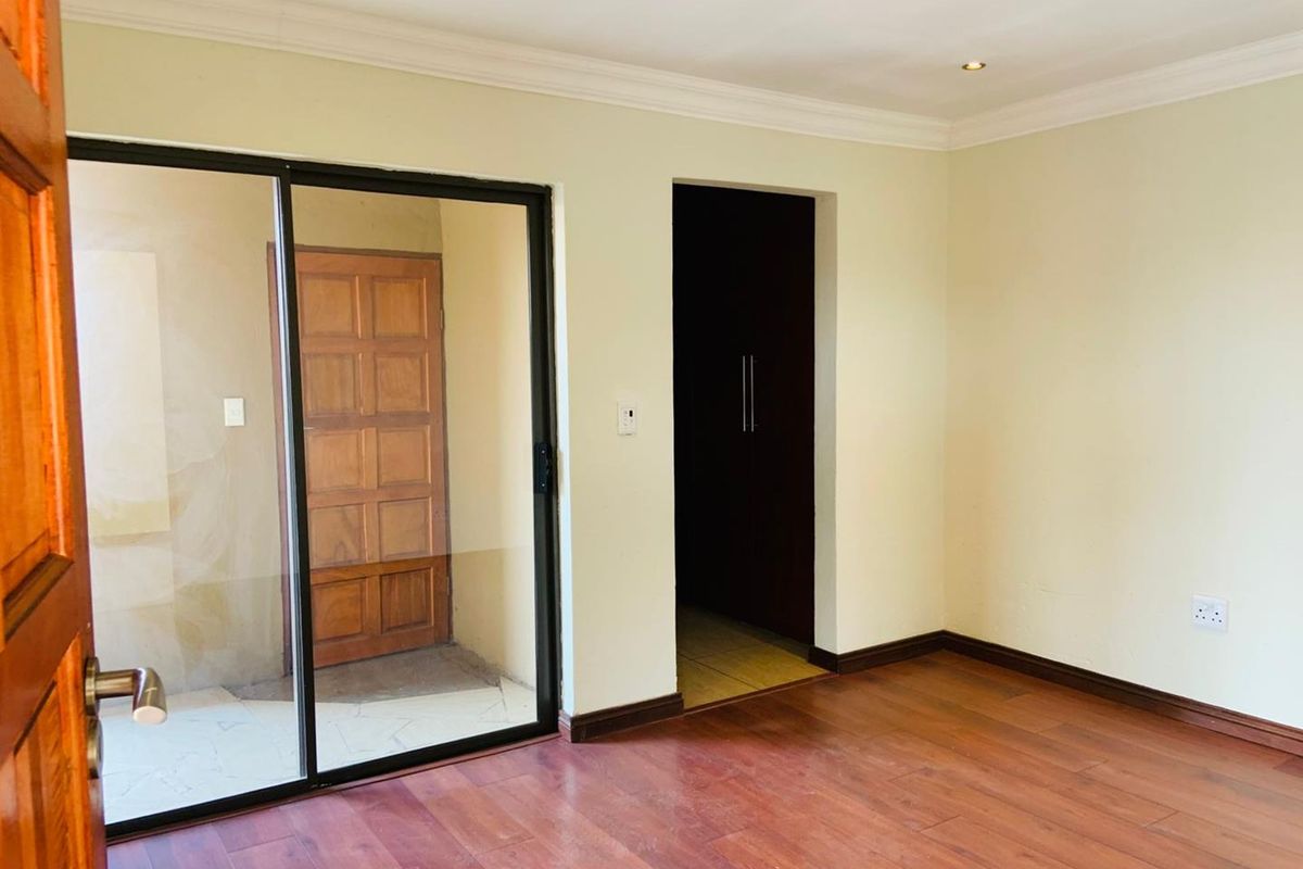 A bright, empty bedroom featuring laminate wood flooring, built-in cupboards, and a sliding glass door providing access to an outdoor area.