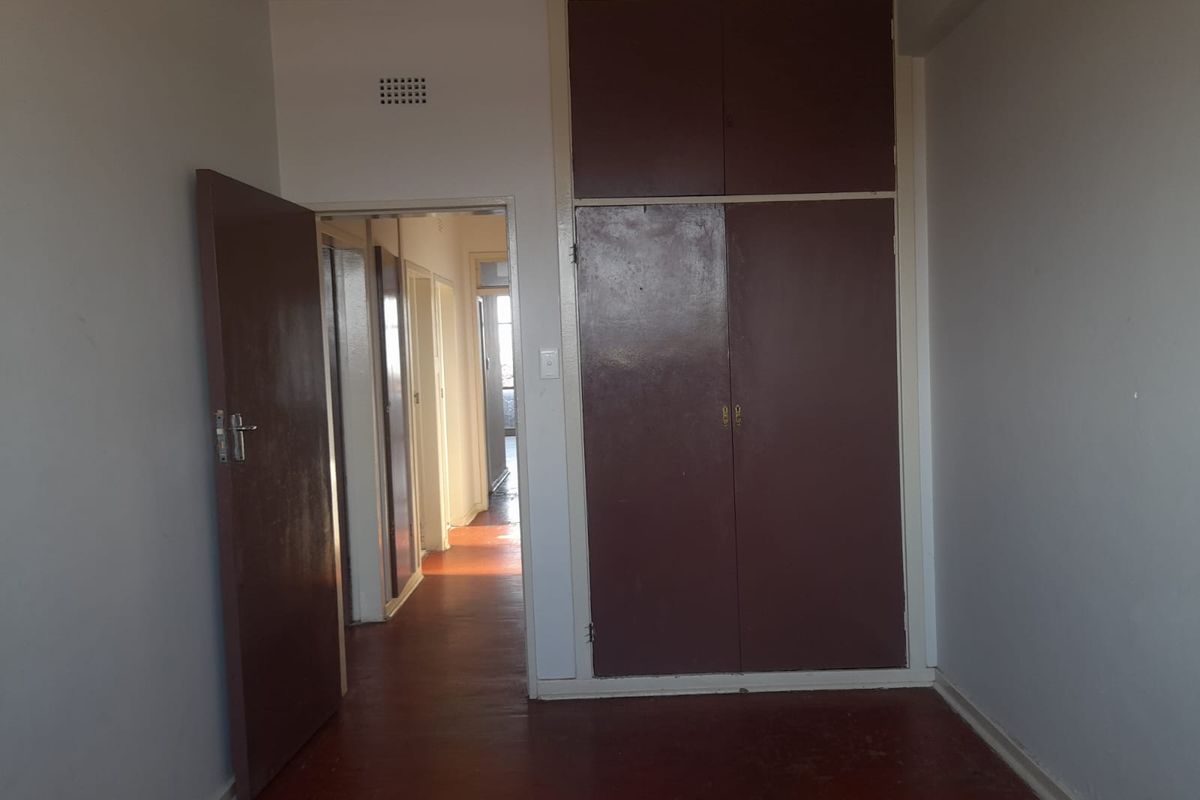 An empty bedroom featuring built-in cupboards and access to a hallway, showcasing original flooring and neutral wall finishes.