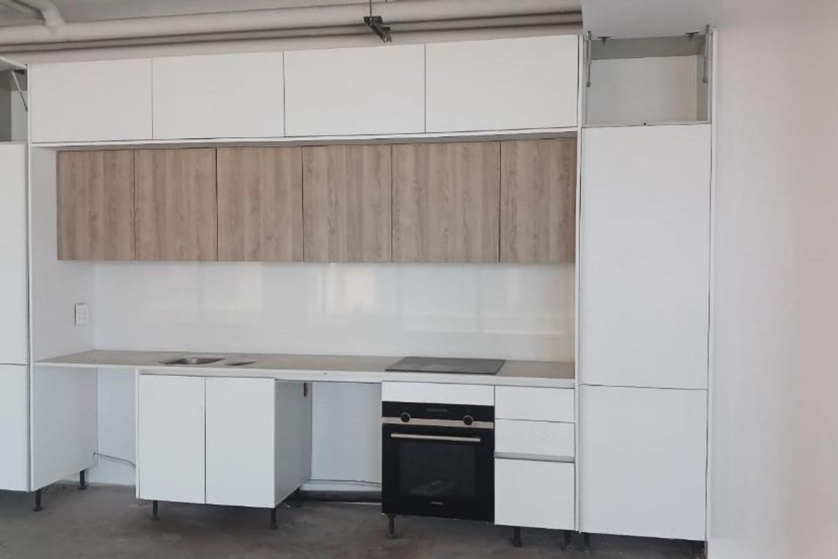 A modern kitchen kitchenette featuring white and wood-tone cabinetry, a built-in oven, cooktop, and sink, currently in an unfinished state.