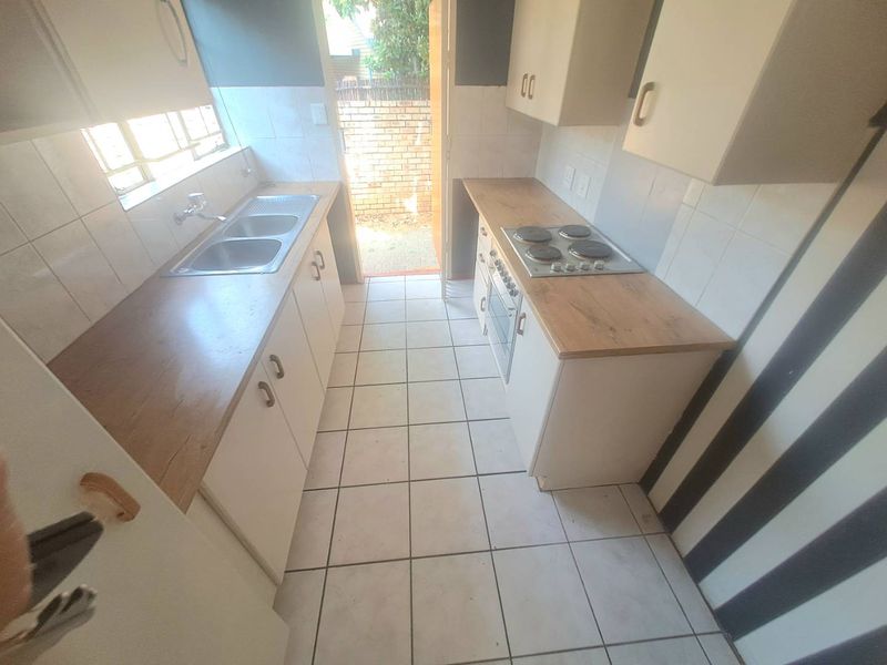 A functional galley-style kitchen featuring built-in cabinetry, a double basin sink, an electric hob, and an integrated oven with direct access to the rear exterior.