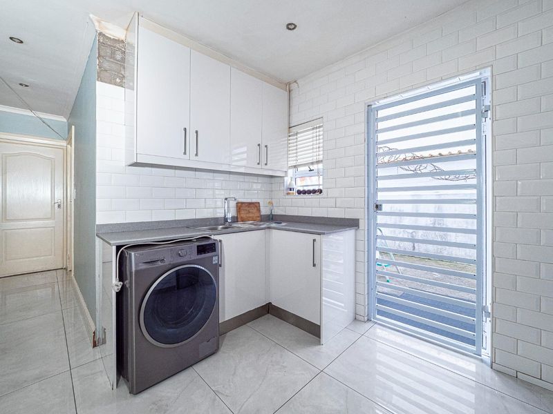 Functional laundry area featuring white cabinetry, subway tile backsplash, tiled flooring, and direct access to the exterior via a security gate.